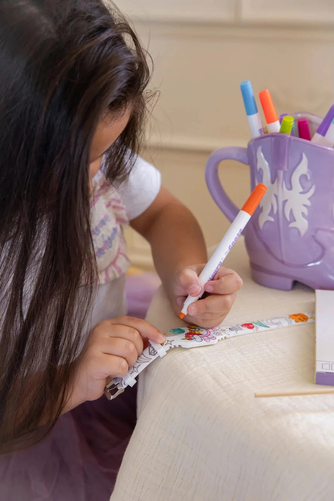 A young girl colors her Henry the Goose digital watch using markers, bringing the design to life with vibrant colors.